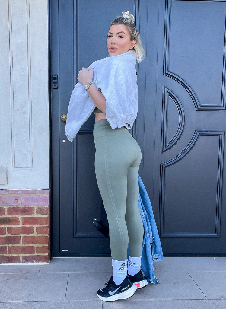 Olivia Bowen stands outside wearing the Seamless Set in Sage Green, with a grey Sweatshirt, and black gym trainers.