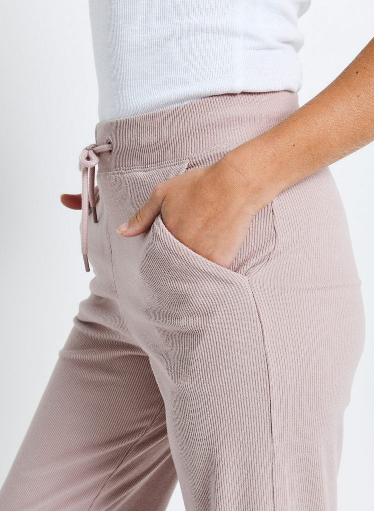 Close up image of light pink loungewear trousers. Model has hands in their pockets.