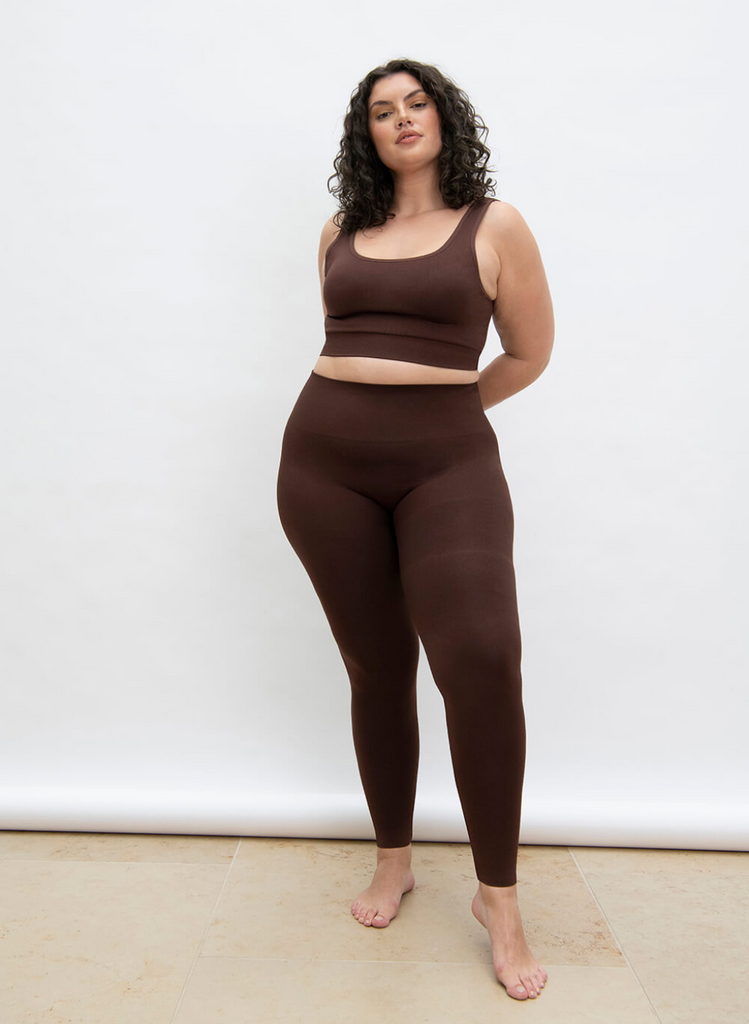Woman stands in studio, against white backdrop, wearing the Chocolate Brown Seamless Set in Curve.