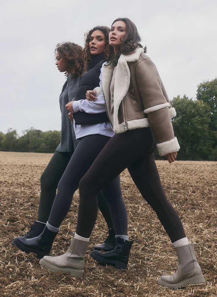 Three Models walking side onto the camera, through a autumnal feild, wearing the Everyday Winter Leggings by LOVALL. They are wrapped in winter coats and boots.