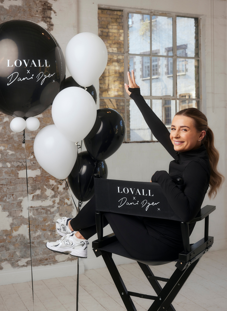 Dani Dyer wears the Empower Set in Black, sitting on her LOVALL X Dani Dyer branded chair, with a branded balloon to match.