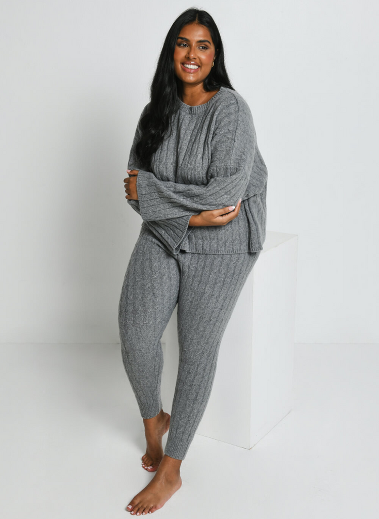 Model sits on block wearing the Cable Knit Joggers and Jumper in Grey.