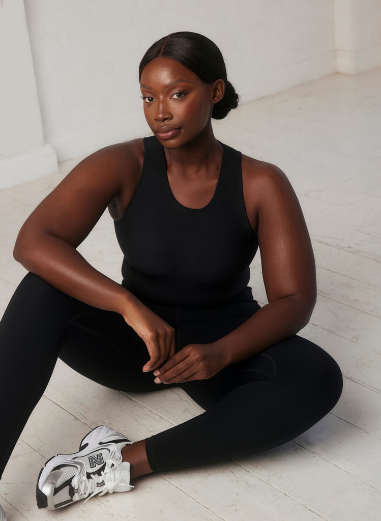 Woman sits on the floor wearing the Empower Black Top and Empower Black Leggings, with running trainers.