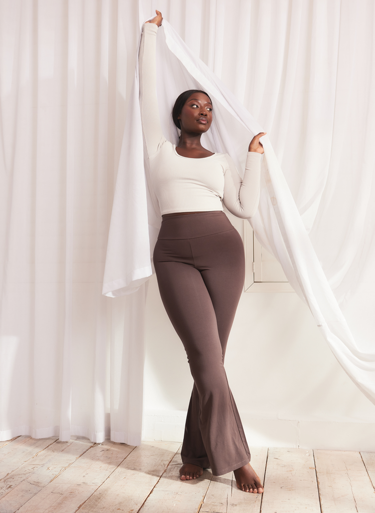 Woman stands holding mesh curtains wearing Espresso Brown Lightweight Flare Leggings and a grey top.