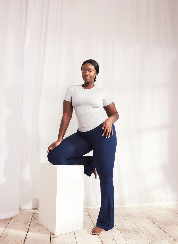 Woman stands with one leg up on a block, she wears the Navy Lightweight Flare Leggings and a grey t-shirt.
