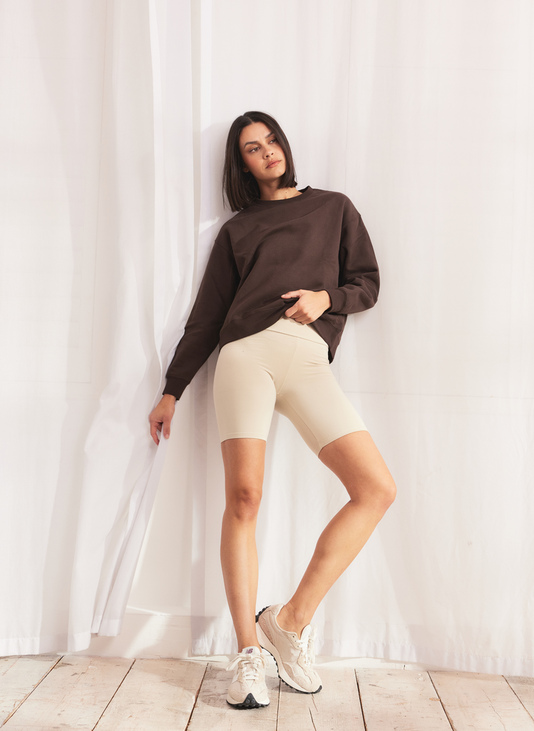 Woman wears Beige Cycling Shorts and Brown Jumper.