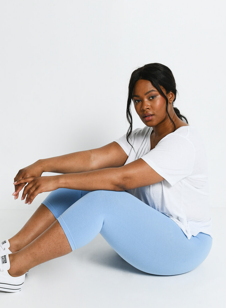 Model sits on the floor wearing Powder Blue Cropped Leggings and white top.