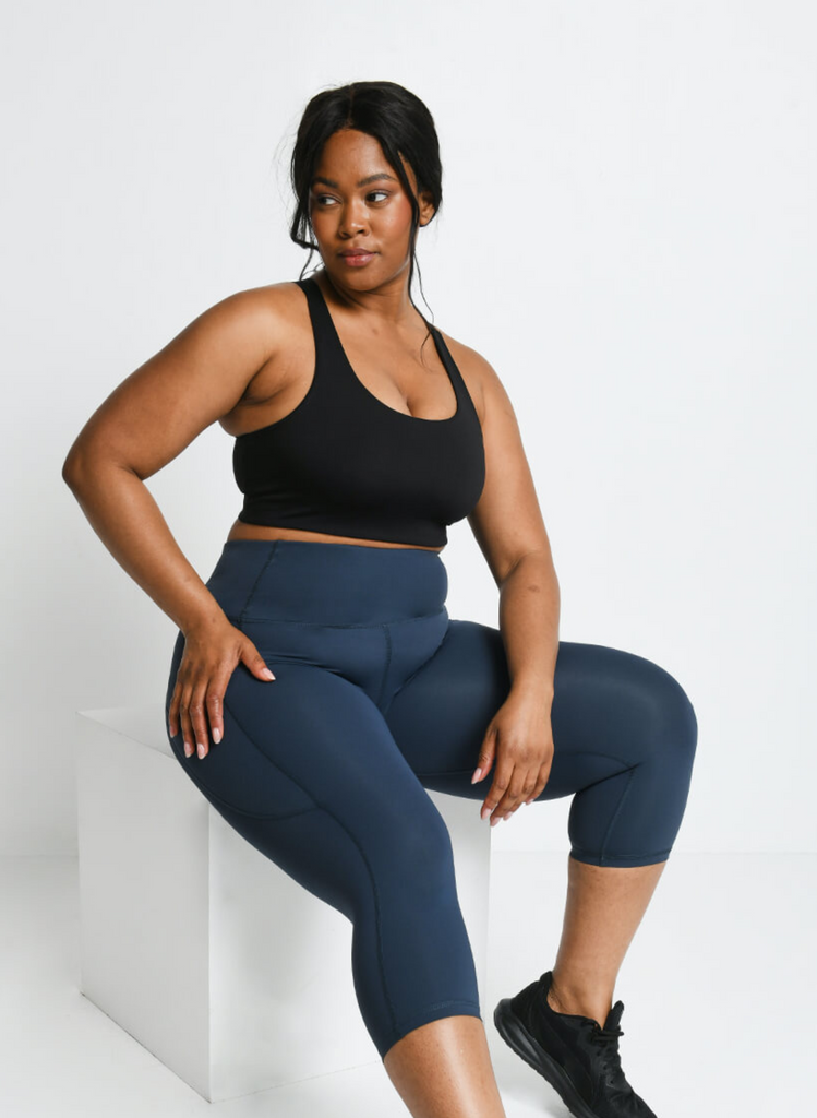 Model sits on a block, wearing Cropped Teal Gym Leggings and a black sports bra.