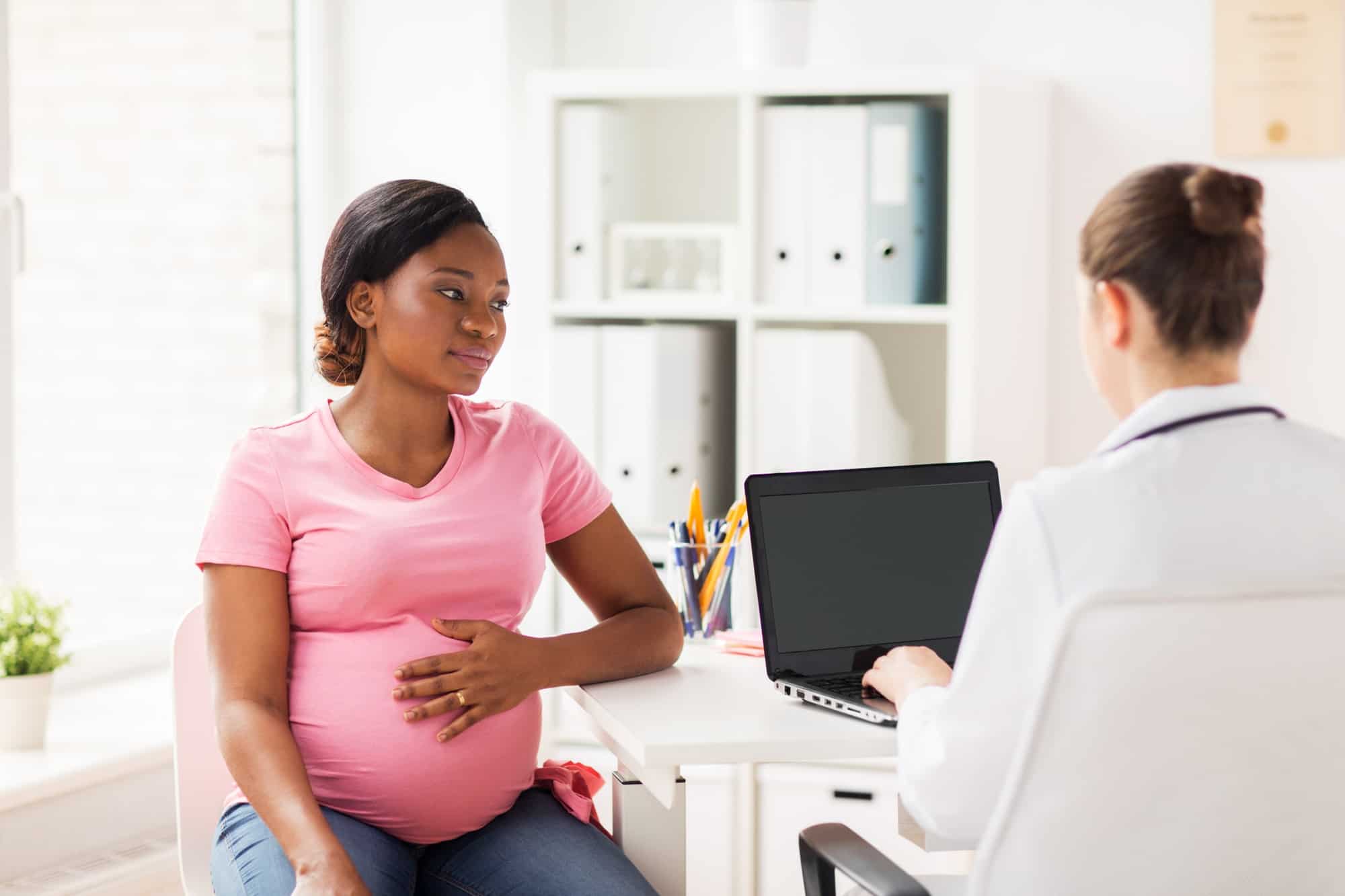 pregnant woman with third trimester nausea talking to doctor at clinic