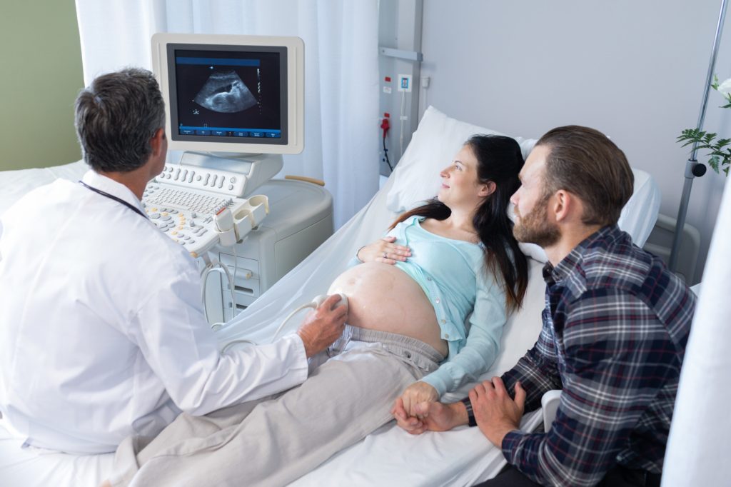 High angle view of Caucasian male doctor doing ultrasound scan for pregnant woman in hospital