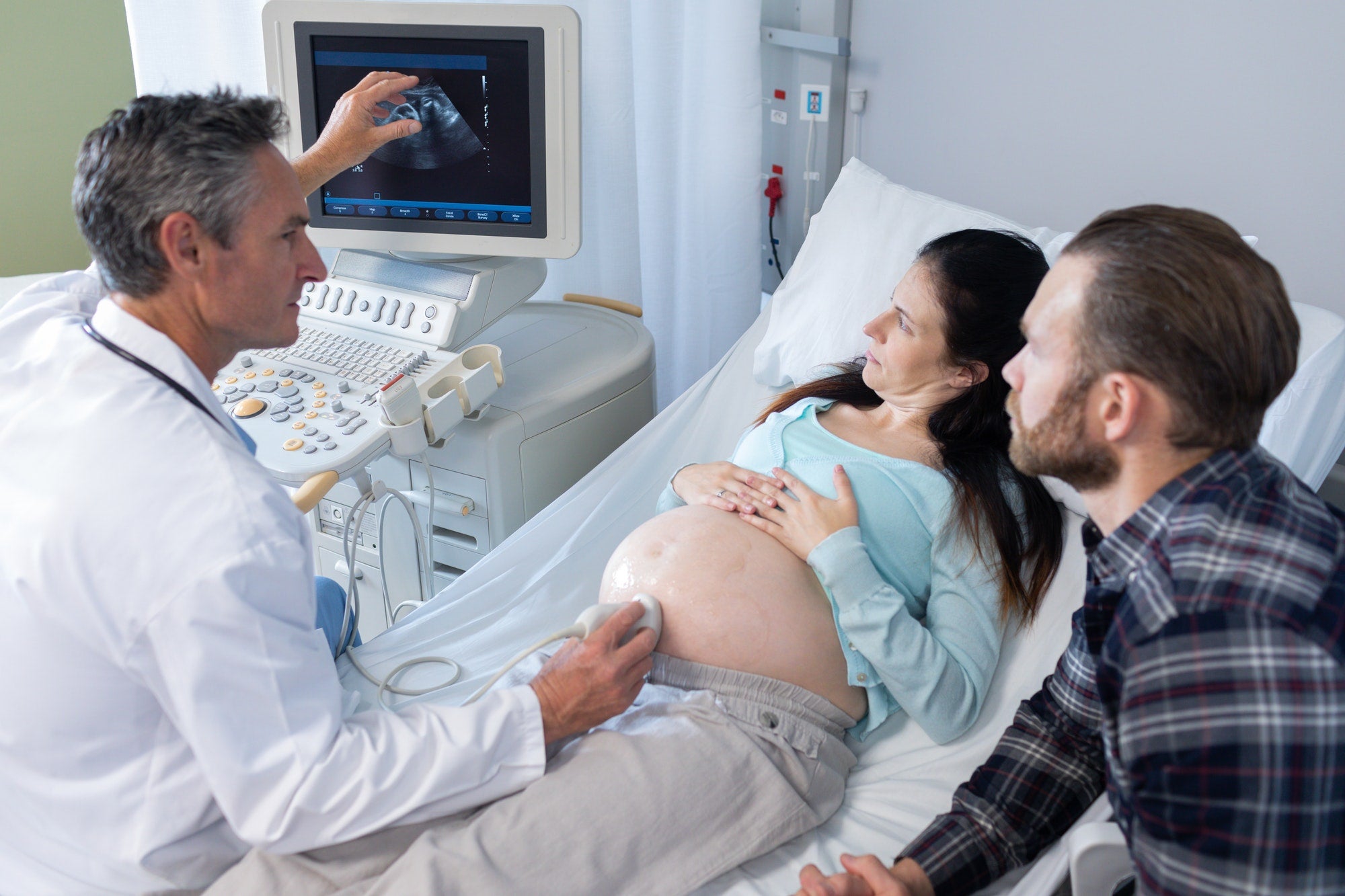 Side view of Caucasian male doctor doing ultrasound scan for pregnant woman in hospital