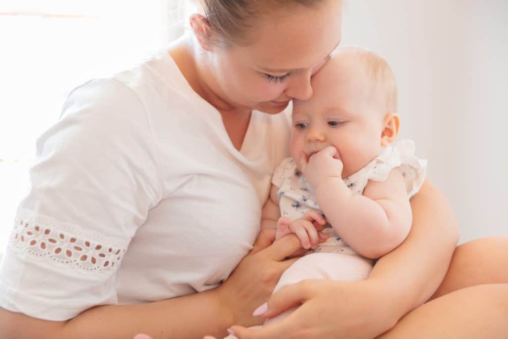 Smiling mom cares for her little sad baby girl