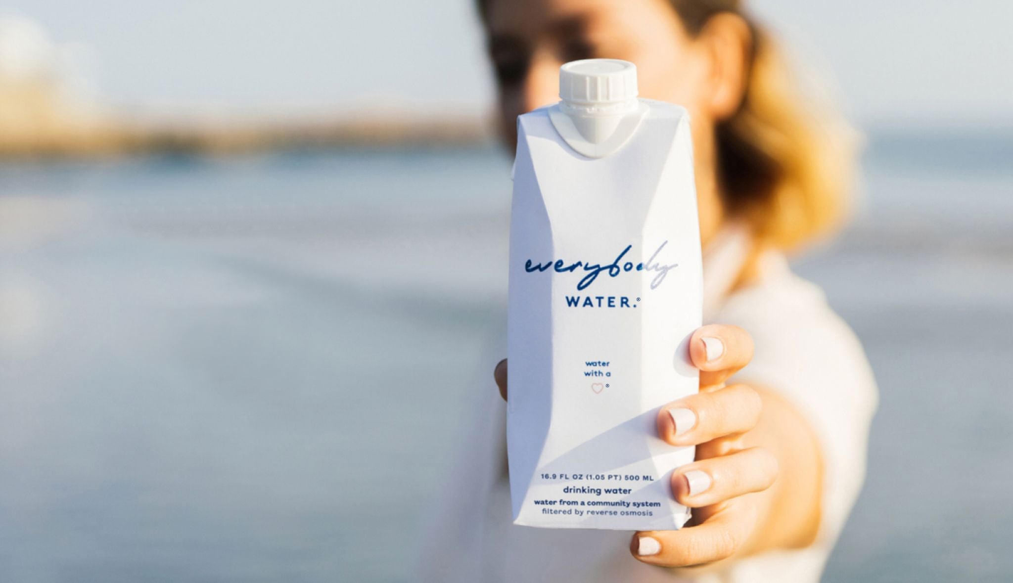 Charlotte holding a carton of everybody water on the beach