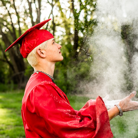 Teenage boy in red graduation robes throwing white powder