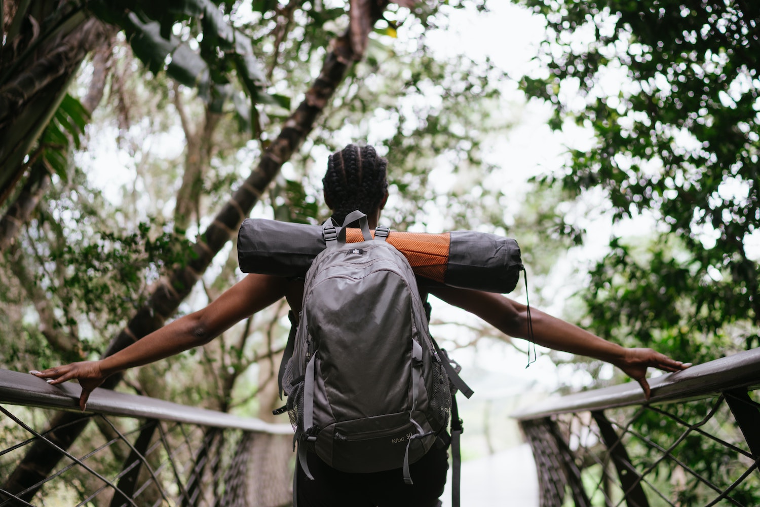 Hiker carrying backpack across bridge