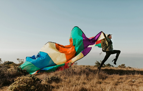 Pattie waves a billowing rainbow flag in an open, outdoor landscape