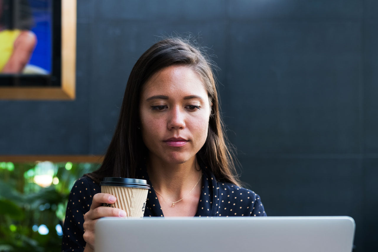 Woman holding coffee looking at laptop screen