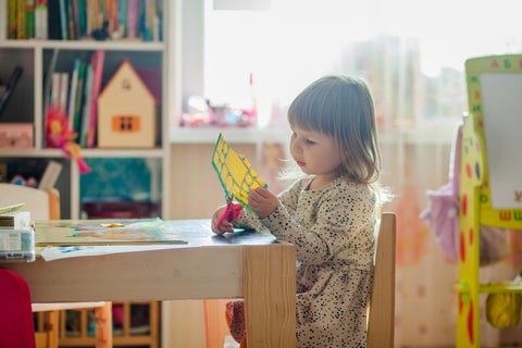 child sitting at a table using scissors to cut