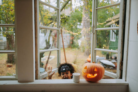 pumpkin on windowsill with child shouting boo though window