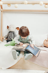 little boy reading a book on his bed 