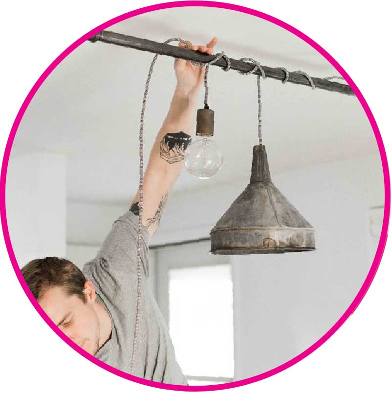 Man hanging a DIY lighting project with cloth-covered cord and rustic metal shade