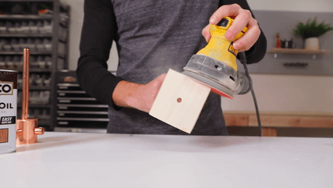Person sanding a piece of wood over a workbench