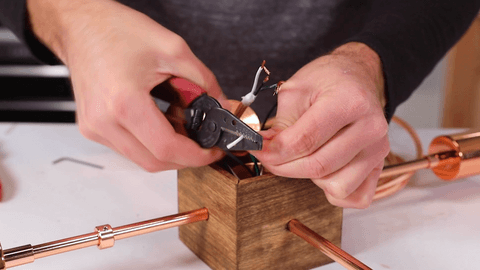 Hands cutting wire over a wood and bronze light fixture