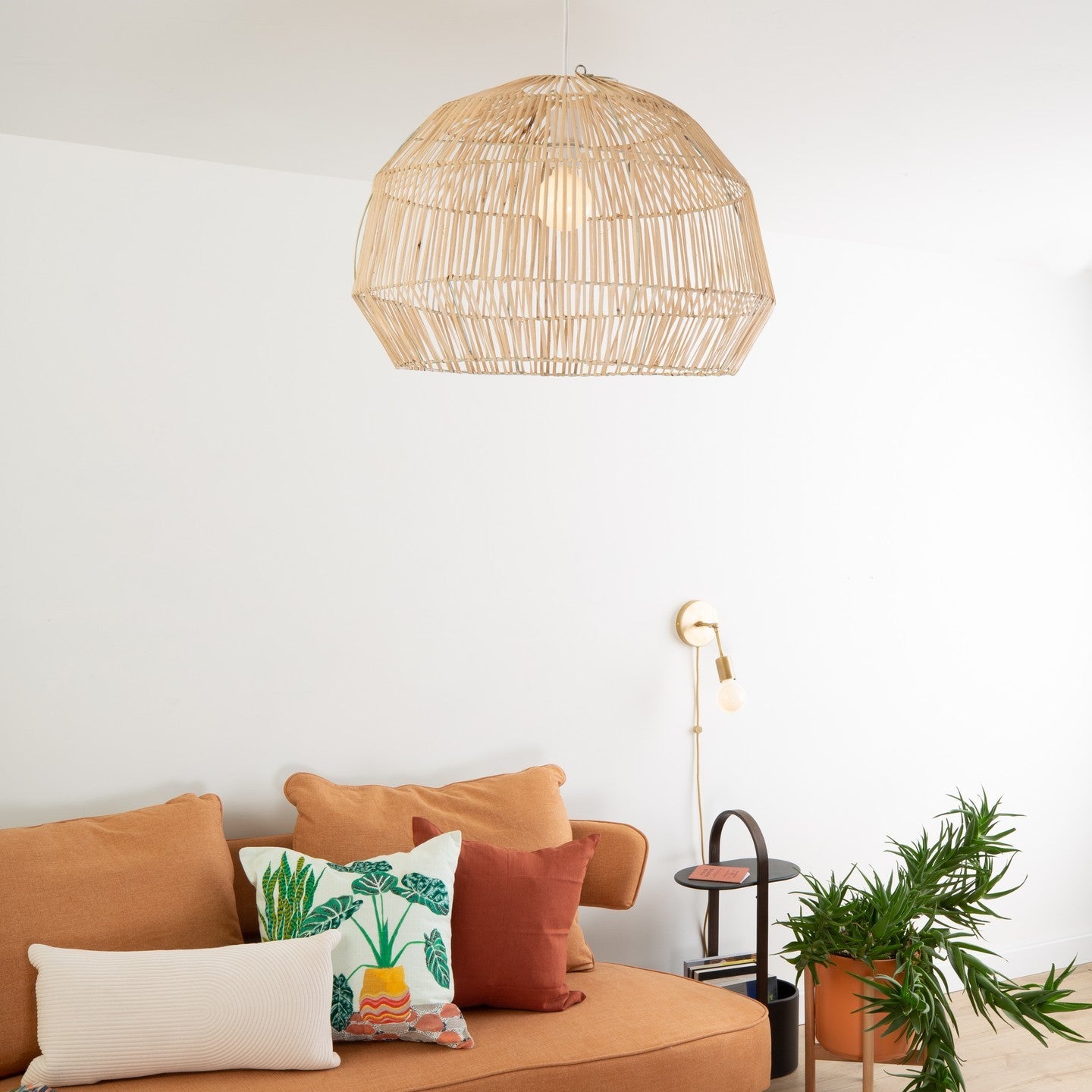 Layering Color Cord Company’s woven basket shade ceiling pendant with wall sconce in a reading nook featuring orange sofa, throw pillows, and plant
