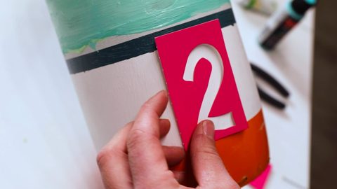 Hand holding '2' stencil over a painted object