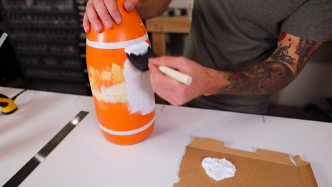 Person with tattooed arm painting an orange container white