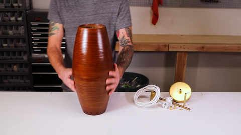 Person holding cylindrical wooden light fixture on workbench