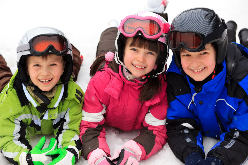 Three children wearing winter gear and helmets