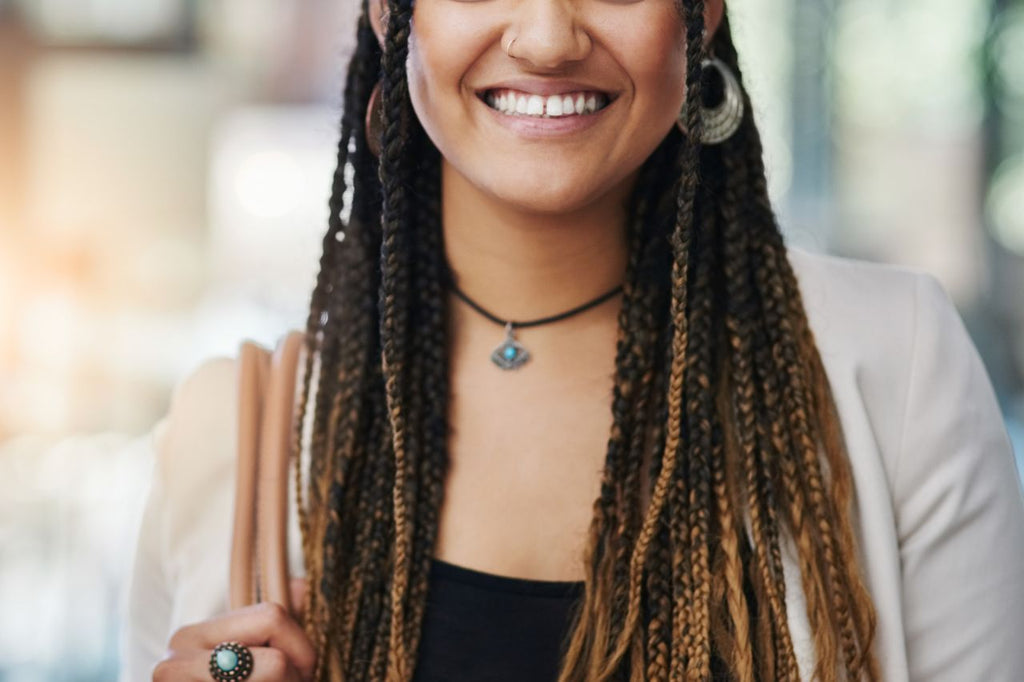 Smiling woman with braids, Cannabis sativa theme necklace.