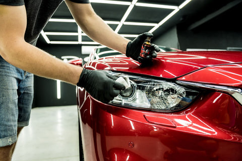 A man carefully paints the headlight of a red car, an essential step in car maintenance and detailing