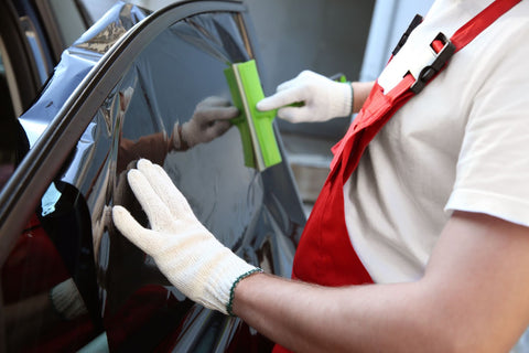 A man in a white apron cleans car window, applying Nano Ceramic Tint to protect against UV rays