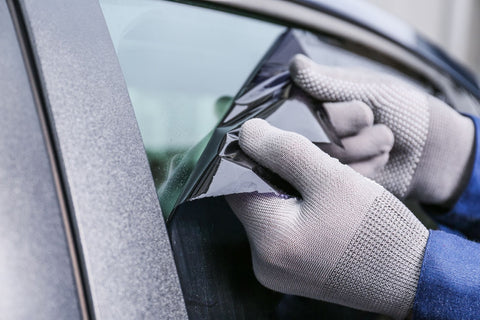 A person expertly applies Nano Ceramic Tint window film to shield a car from UV rays, wearing gloves