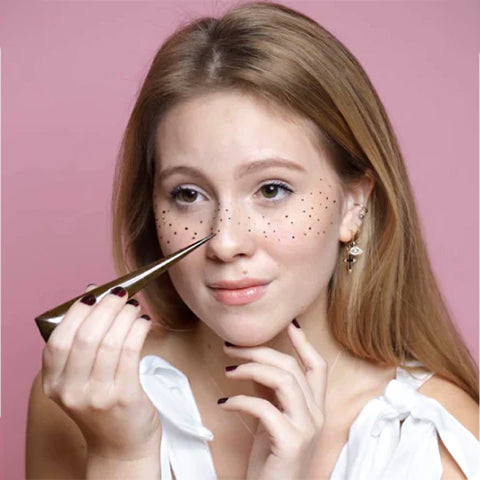 A pretty woman making fake freckles using henna on her face.