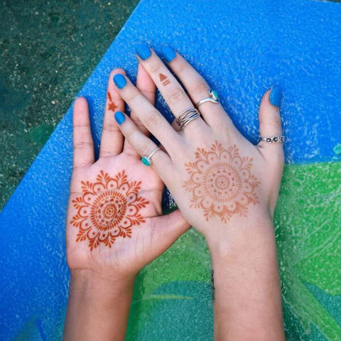 A Woman’s hands adorned with mandala henna designs & complimented by blue nail paint.