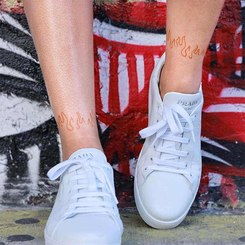 A woman wearing white sneakers with a flame thrower henna tattoo on her lower shin.