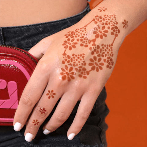 A woman showcasing flower power henna tattoo on her hand & finger, complemented by nails with white nail polish.