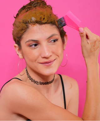 A woman applying henna hair dye paste on her hair using a hair brush.