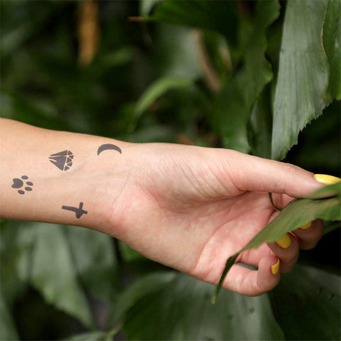 A woman’s arm showing off jagua tattoos including cross, crescent moon, diamond