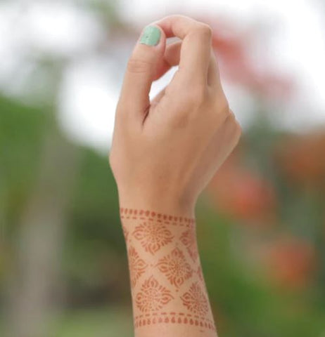 A woman showcasing a geometric henna tattoo on her arm complemented by green nail paint.