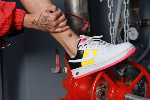 A woman wearing white sneakers with pink bottom adorning jagua tattoos on her arm & leg.