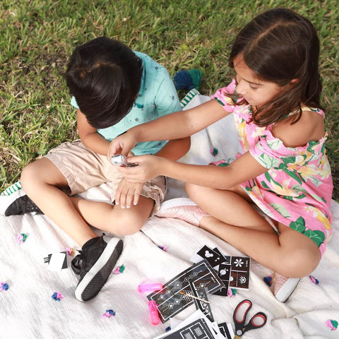 Two kids applying tattoos using a henna cone and a pack of stencils.