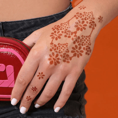 An image of a woman’s hand with a flower power henna design at the back of her palm.