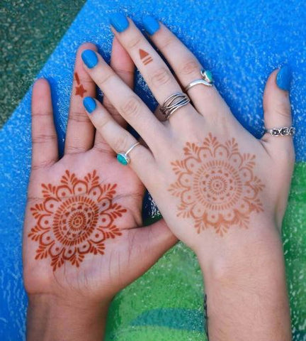 The image represents reddish-brown mandala tattoos on the front and back of a woman's palm.