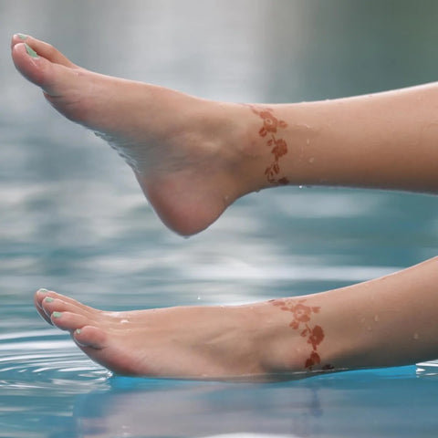 A woman's feet wrapped in floral henna designs and dipped in a pool.