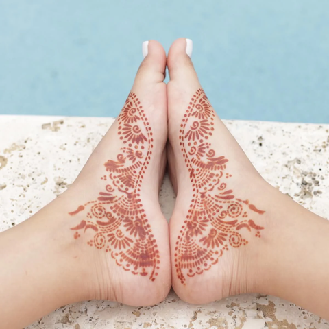 A woman adorning her fawn henna design on her feet.