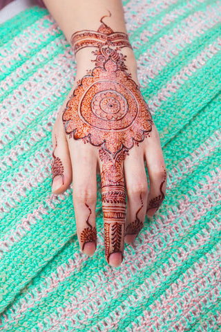 A woman adorning a mandala henna design on the back of her hand. The design is complemented by finger designs.